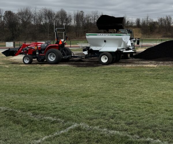 Spreader is filled by a loader to top dress Central Dauphin School east athletic fields